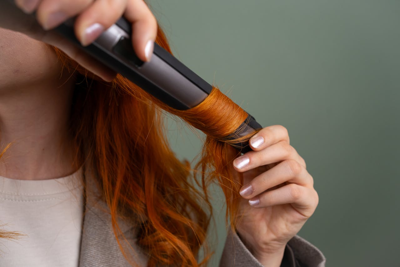 Close-up of a woman curling her vibrant red hair with a curling iron.